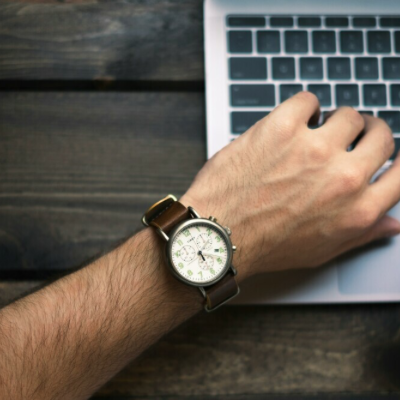 A man looking at his watch while working on his laptop