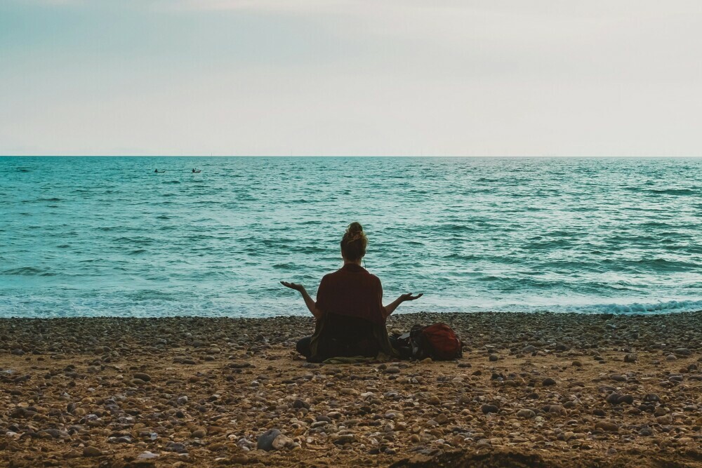 A lady meditating on a beach in front of the sea