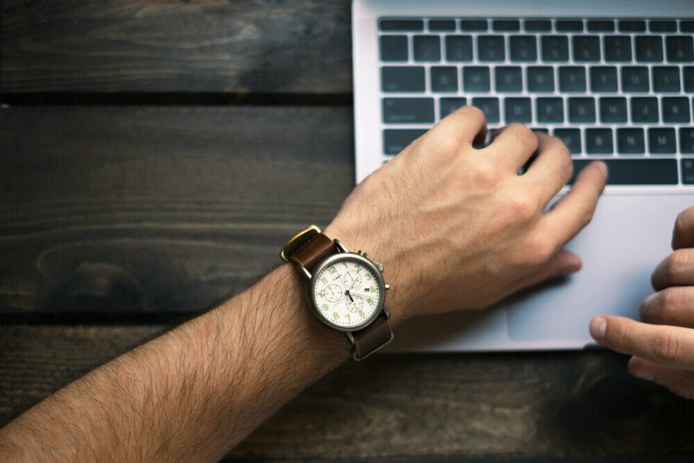 A man looking at his watch while working on his laptop